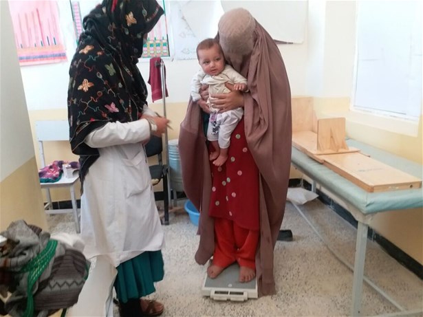 A nutrition counsellor weighs a mother and child at a health clinic in Zabul province