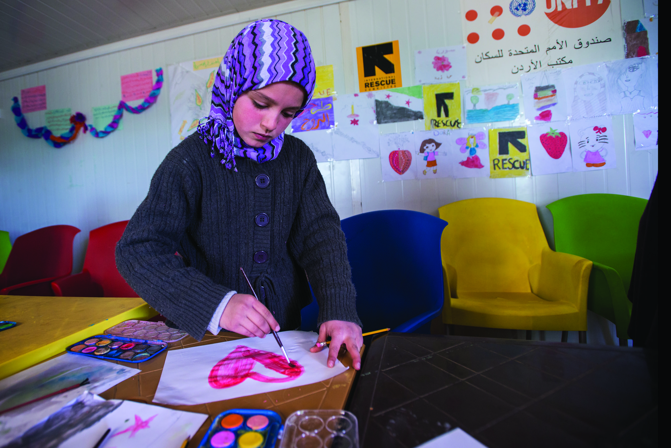 A Syrian refugee girl paints at a children’s play area at an IRC women’s center at Zaatari camp.