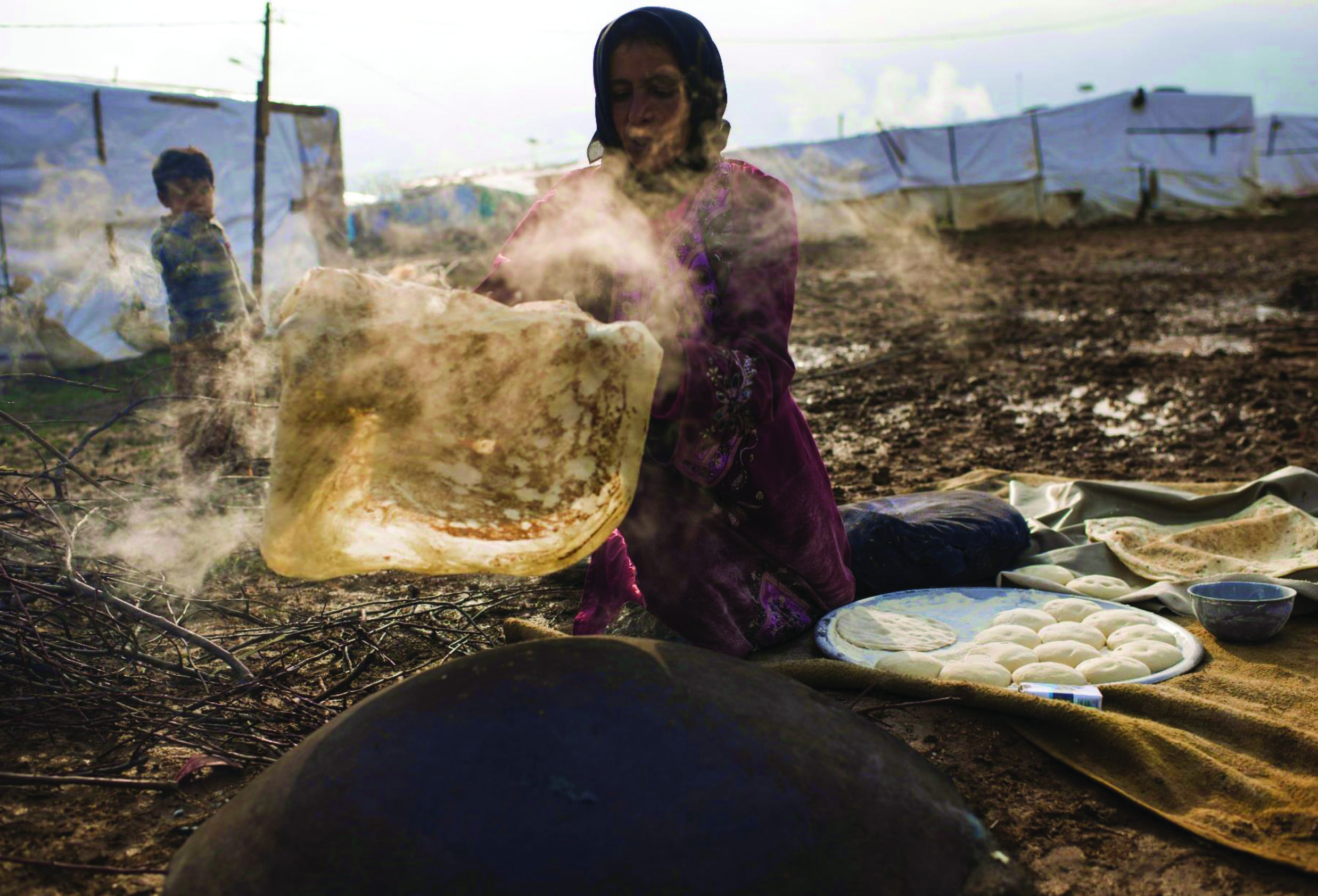 A Syrian mother from Homs, Syria bakes bread outside her shelter in Turbide, Bekaa, Lebanon