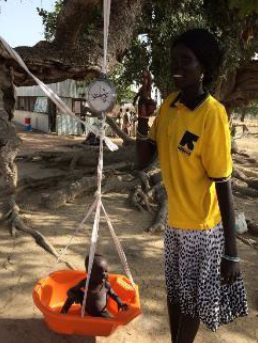 A CHW weighing a child to determine the daily dosage of RUTF