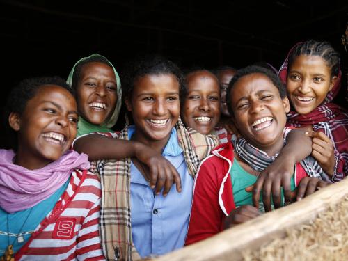 A group of adolescent girls smiling in a window of their school in Ethiopia
