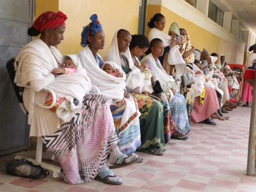 women and their babies sat in a line in a medical facility 