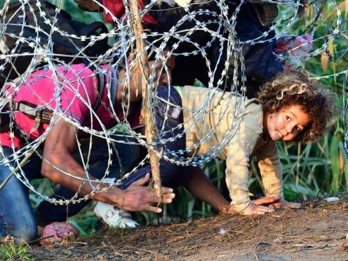 child refugee crawls under barbed wire