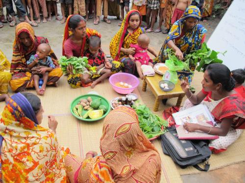 children and women in saris sit on a mat with food arrayed in front of them