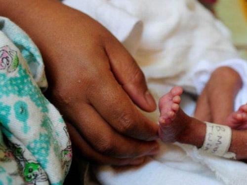 woman's hand touches the foot of a premature newborn baby