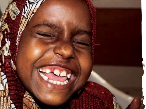 Image shows a child smiling and showing their growing teeth.