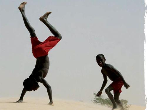 Image shows two children running and playing in the sand. One of them is doing a cartwheel.