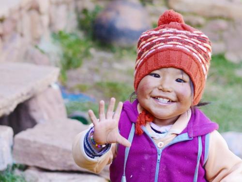 A child in a woolly hat waving at the camera