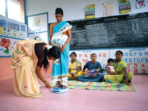 Girls being weighed in a classroom by the teacher