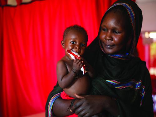 Mother holding child who is eating RUFT.