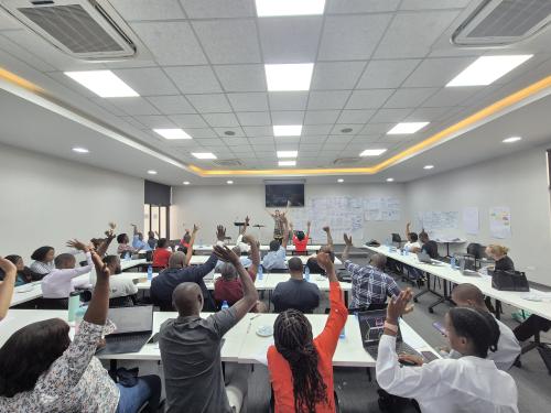 A group of people in a room with their hands up while someone presents at a meeting