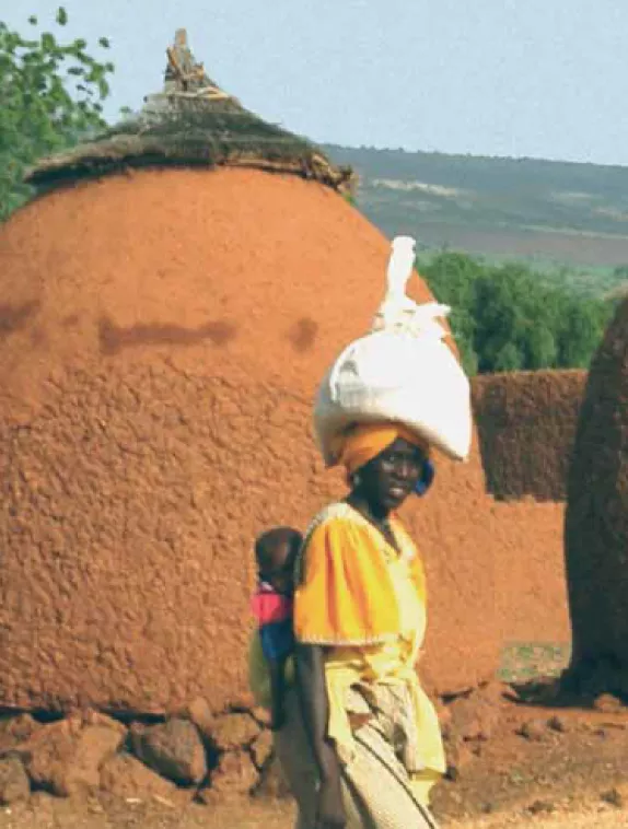 Image shows picture of woman walking with a baby strapped to her back and carrying something on her head