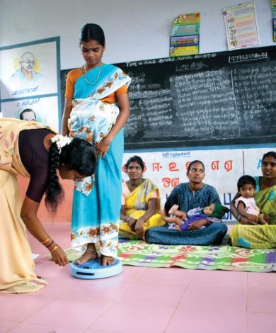 Girls being weighed in a classroom by the teacher