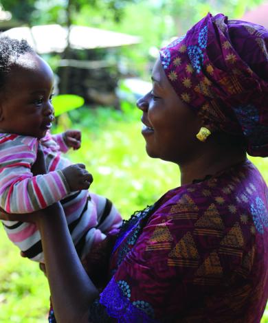 A woman holds an infant up, both are smiling at each other.