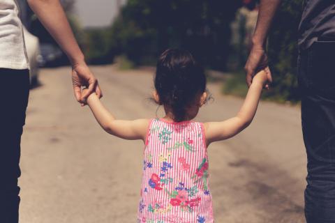 girl walking holding hands with adults on either side