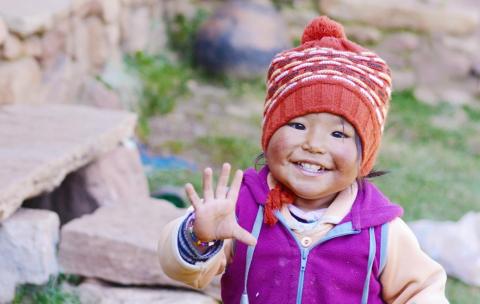 A child in a woolly hat waving at the camera