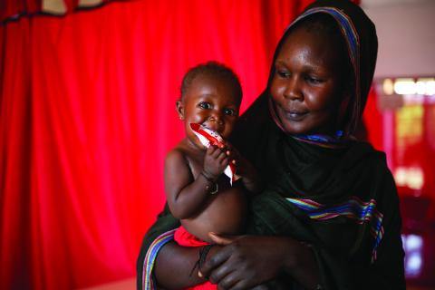 Mother holding child who is eating RUFT.