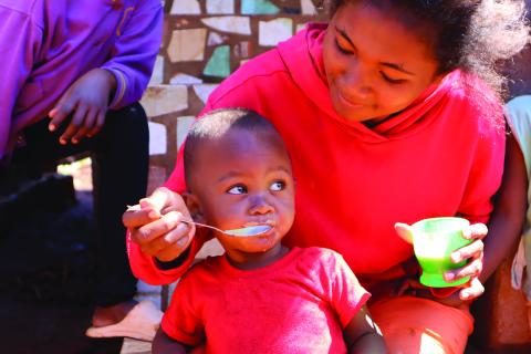 Female wearing a red jumper feeding an infant porridge with a spoon