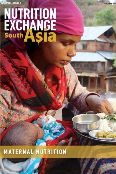Woman holding baby and eating from a tray of food.