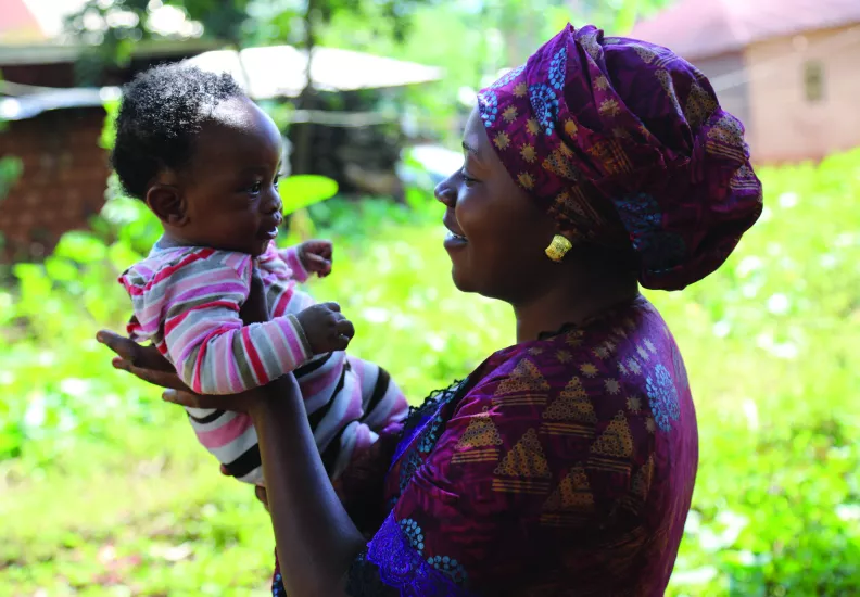 A woman holds an infant up, both are smiling at each other.